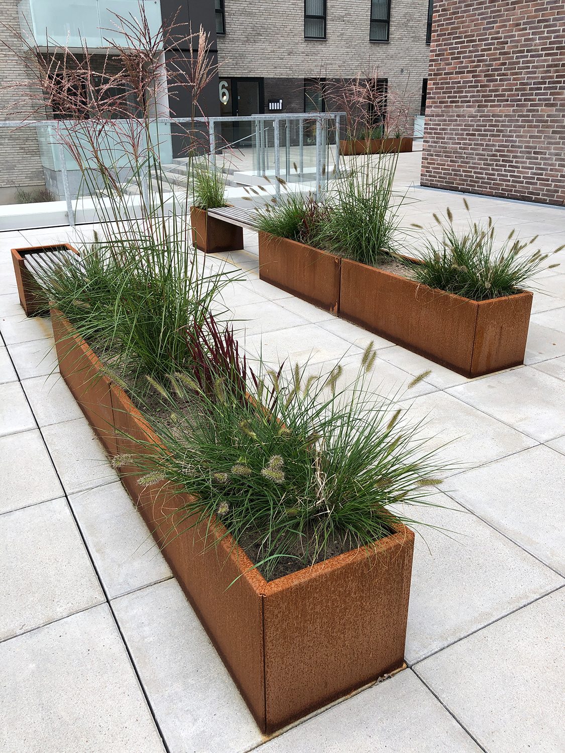 Land Moderna Blomlådor I Cortenplåt Och Bänkar Är Ett Tydligt Sätt Att Skapa En Grön Miljö Mellan Byggnaderna